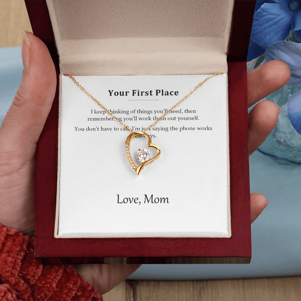 Hand holding the luxury gift box with the gold heart necklace, on a red knitted background