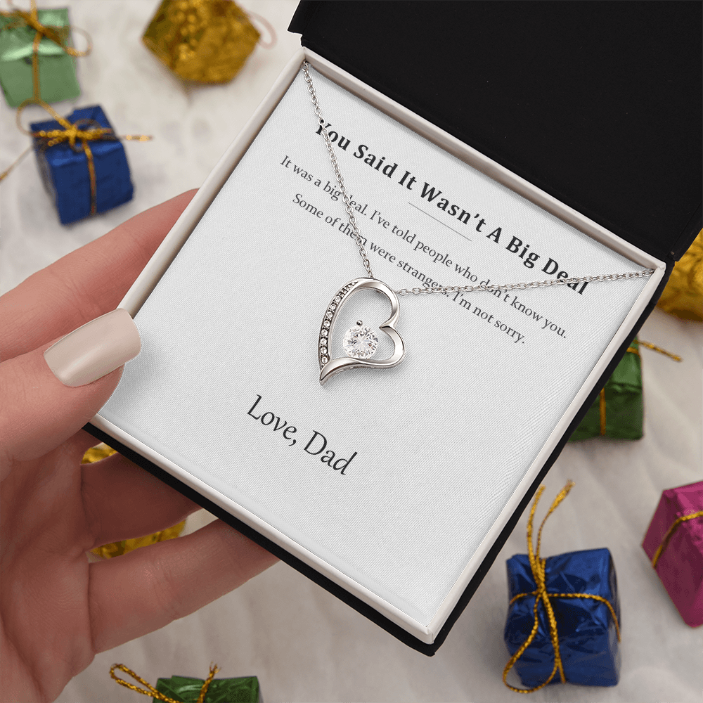 Silver heart necklace and message card held above wrapped presents and ribbon