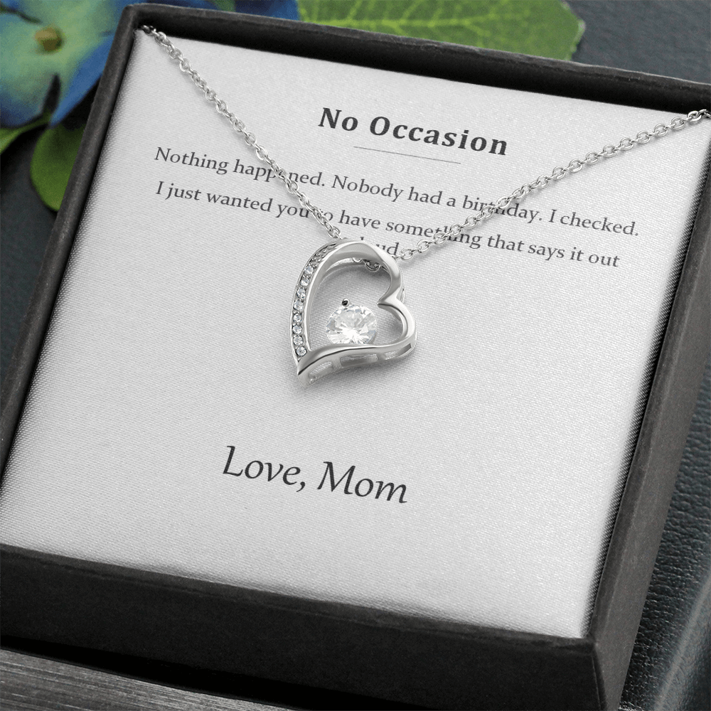 Silver heart necklace on the message card in a black gift box, styled with foliage