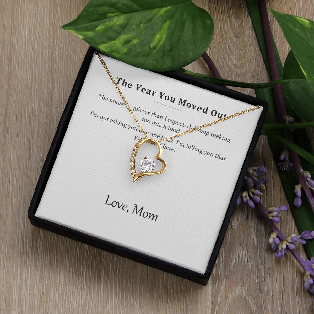 Gold heart necklace and message card in a black gift box beside green leaves