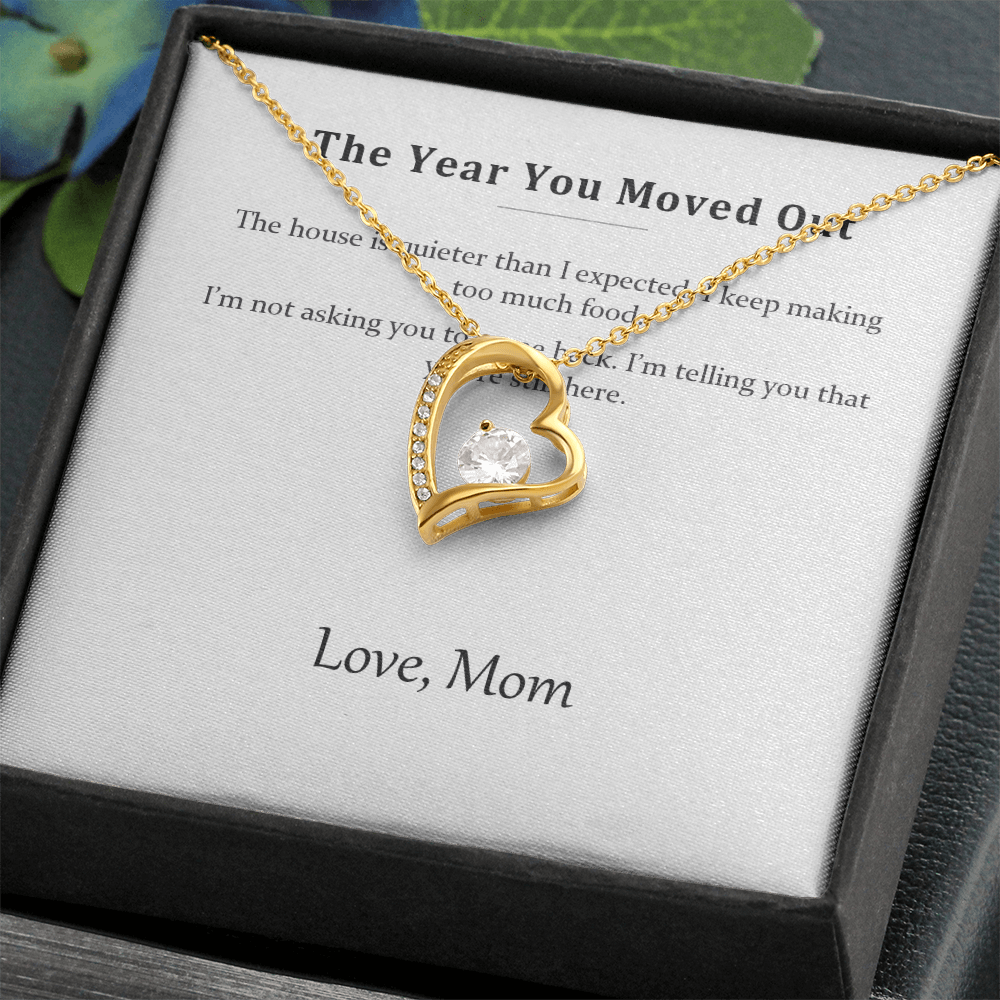 Gold heart pendant resting on the printed message card inside a black gift box