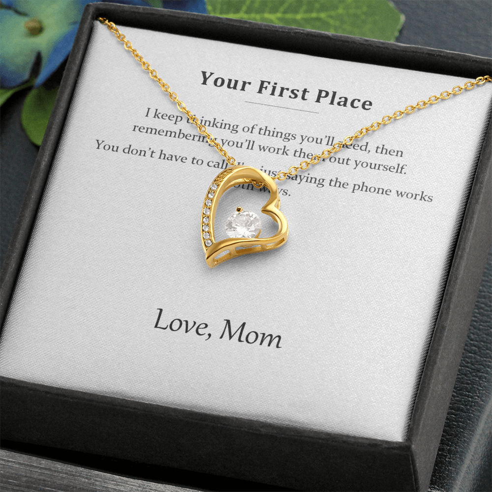 Gold heart pendant resting on the printed message card inside a black gift box