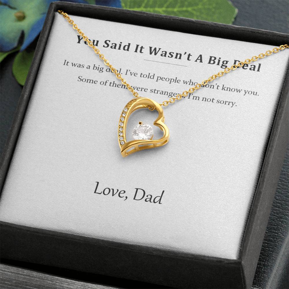 Gold heart pendant resting on the printed message card inside a black gift box